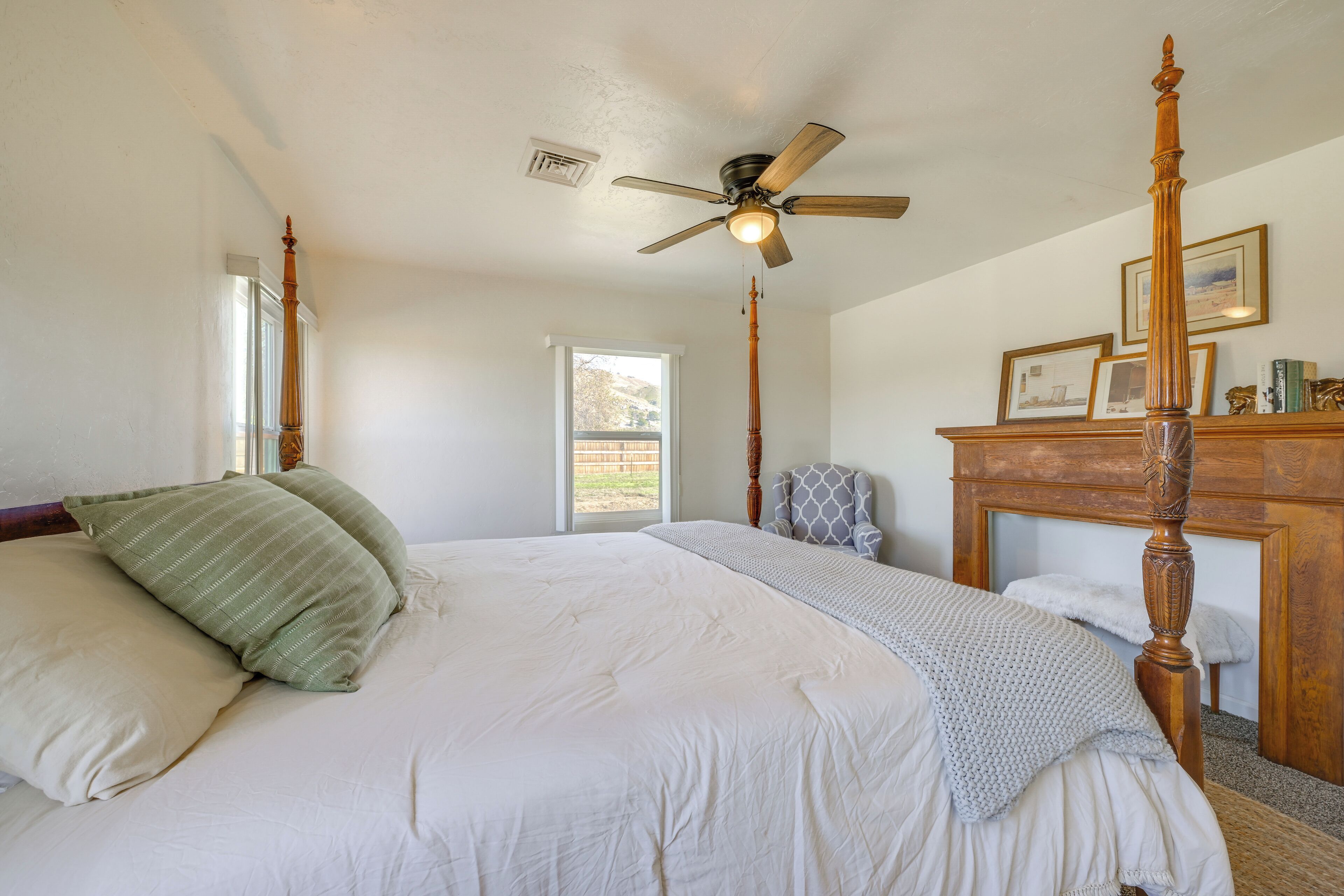 A bedroom with a four-poster bed, a ceiling fan, and a window with a view of a hill.