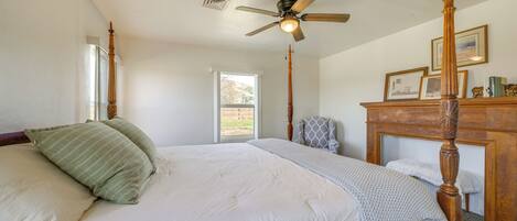 A bedroom with a four-poster bed, a ceiling fan, and a window with a view of a hill.