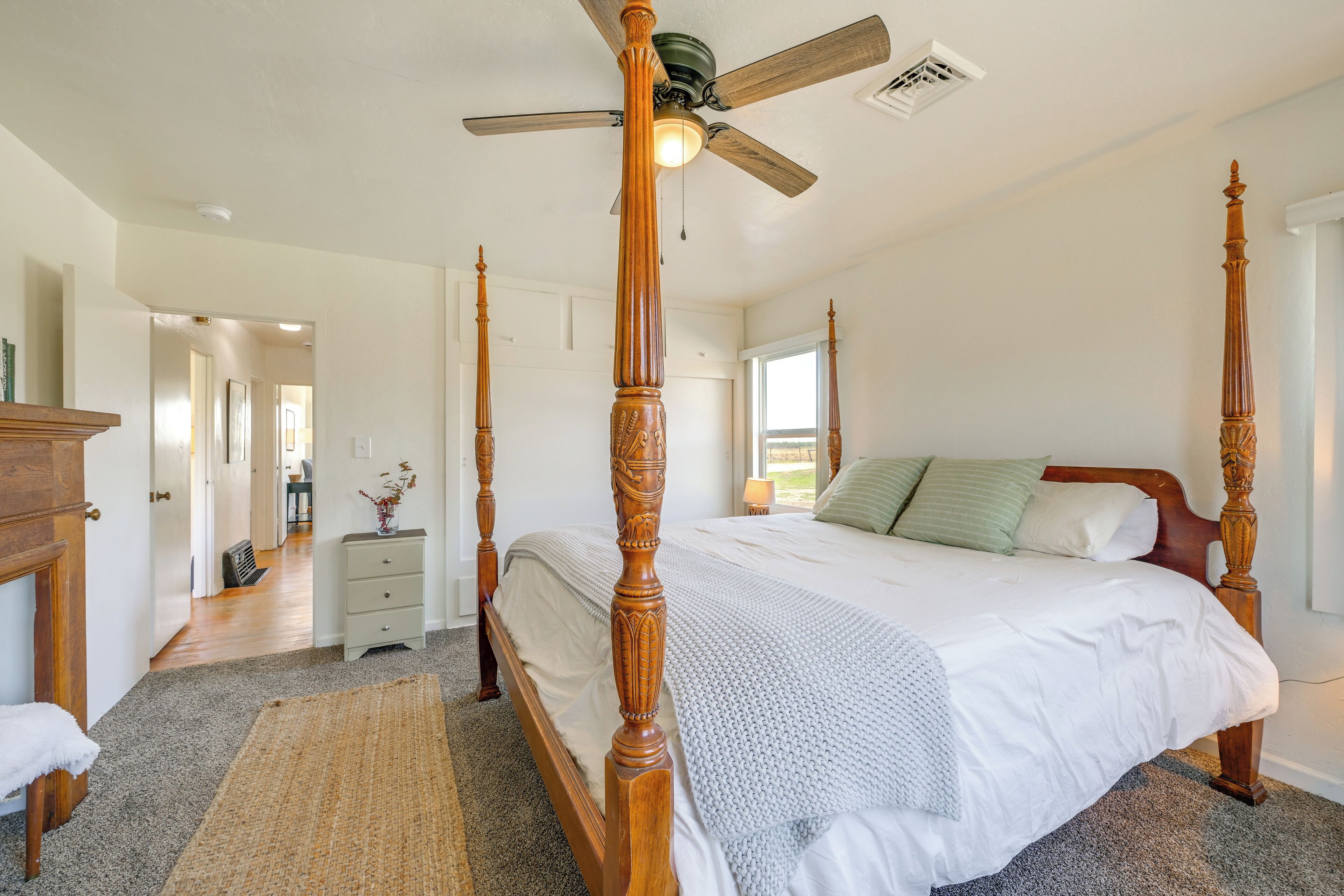Un lit à baldaquin avec une tête de lit en bois, un ventilateur de plafond et une vue sur un couloir menant à une autre pièce.