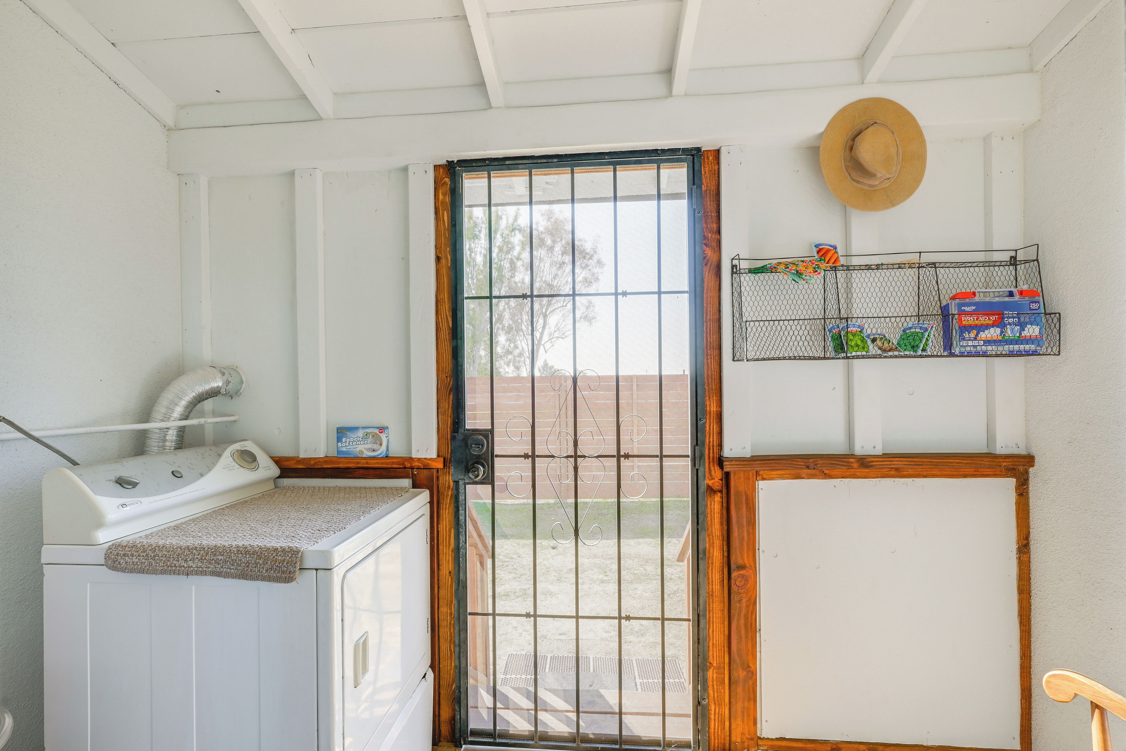 A laundry area with a washing machine, a drying rack, and a metal gate leading to an outdoor area.