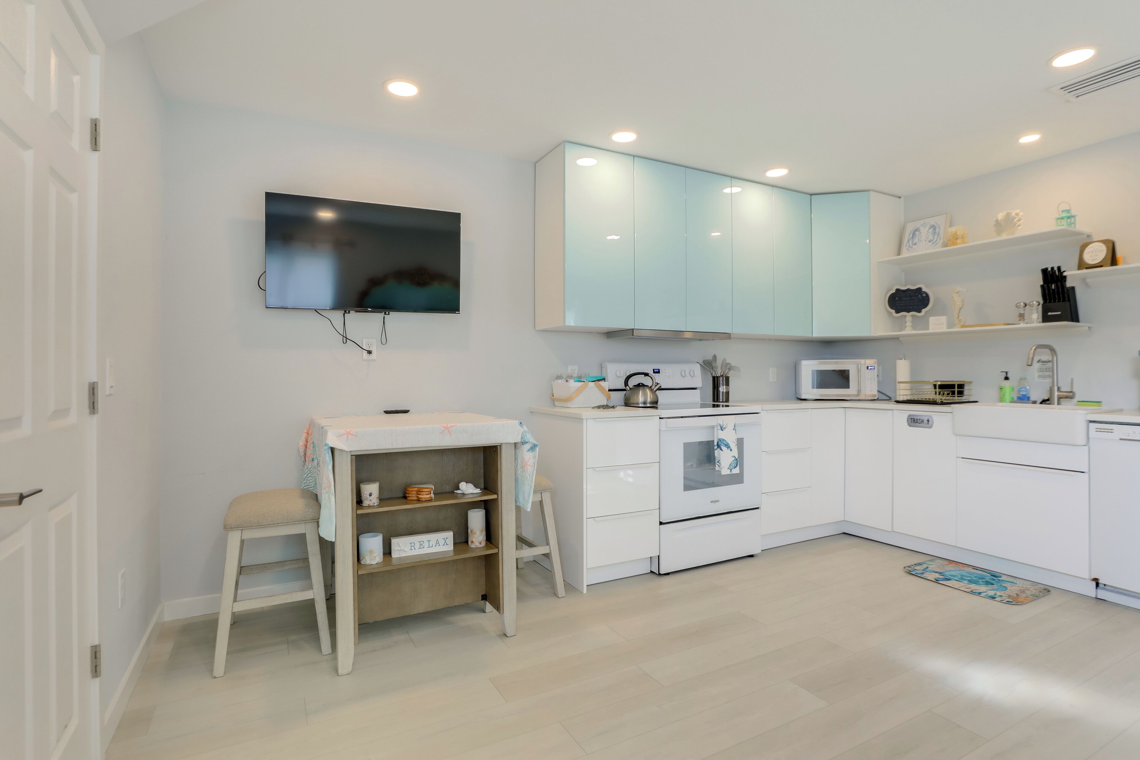 A modern kitchen with white cabinets, a microwave, an oven, and a small dining area with a stool and table.