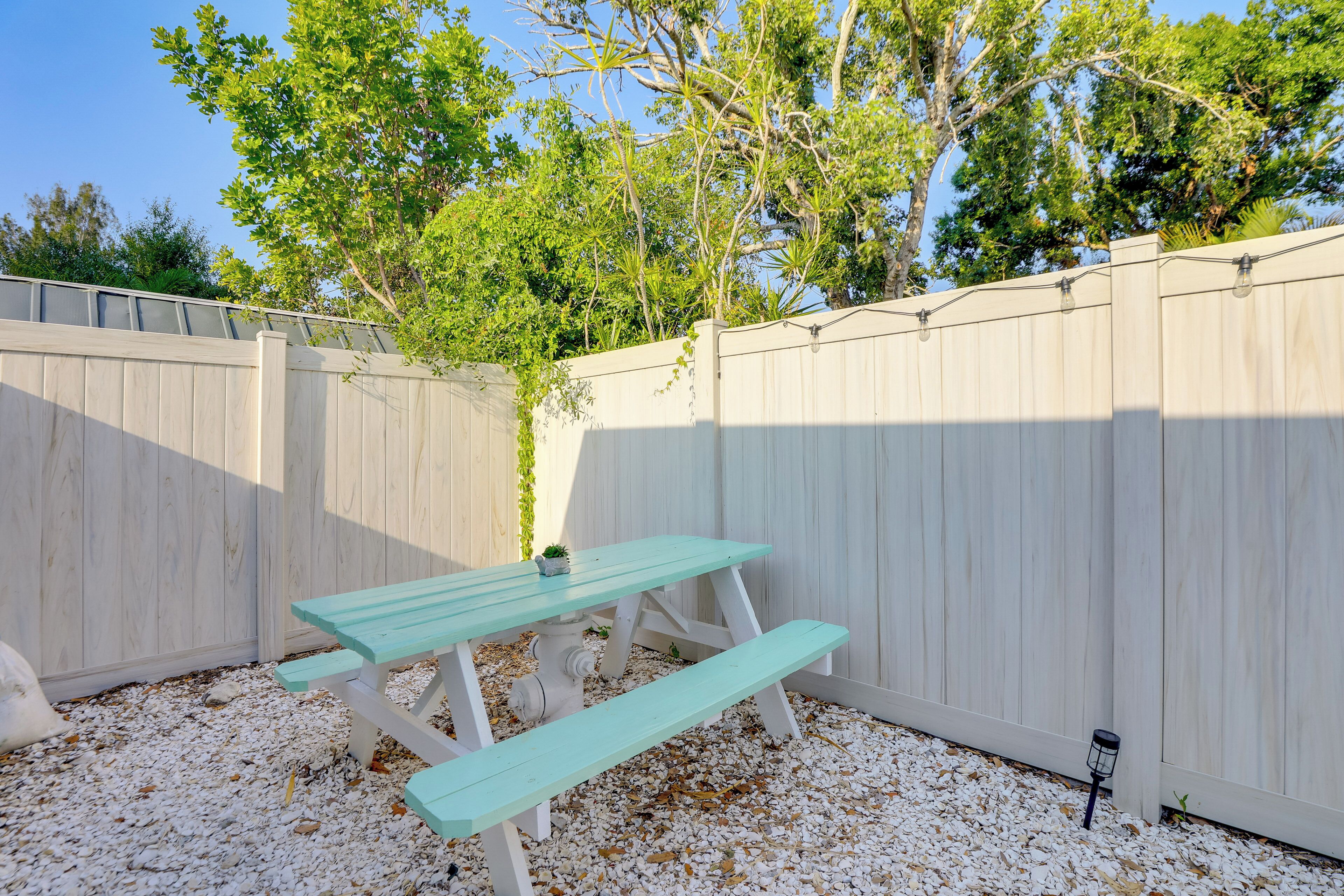 A picnic table with benches in a backyard with a wooden fence and trees in the background.