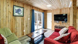Una habitación con paneles de madera, una mesa de madera, sofás verdes y rojos, un televisor y un cuadro en la pared.