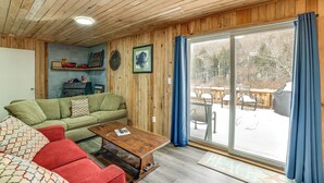Una habitación acogedora con techo de madera, un sofá verde, una mesita de centro de madera y un amplio ventanal con cortinas.