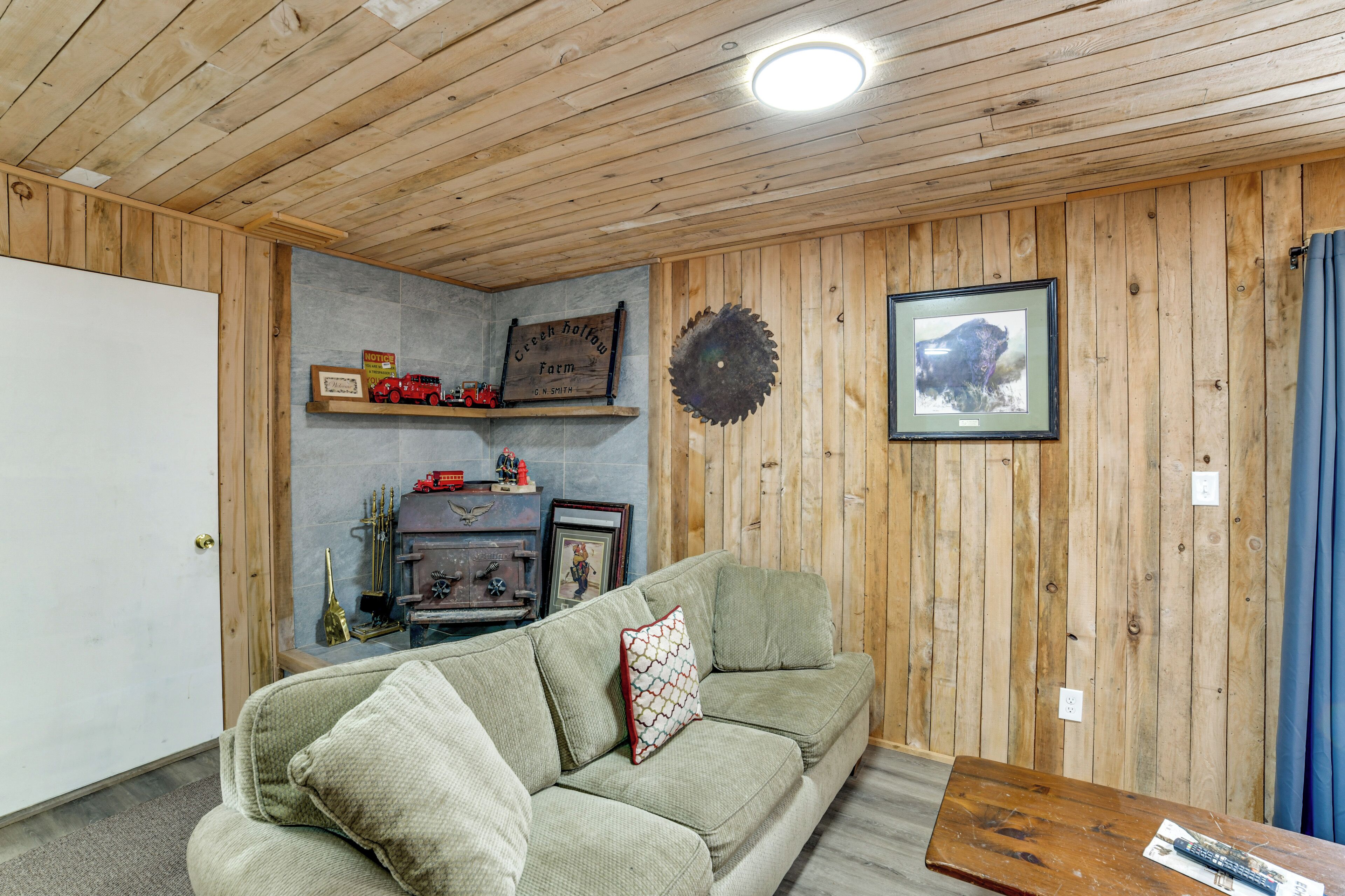 A wooden-paneled room with a green sofa, a small table, and a fireplace with a framed picture above it.