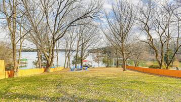 A park with trees, a lake, and a wooden fence.