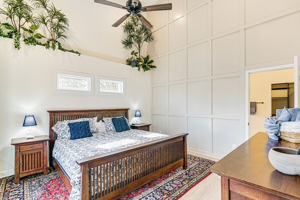 A bedroom with a wooden bed, two bedside tables with lamps, a ceiling fan, and a view of the outside.