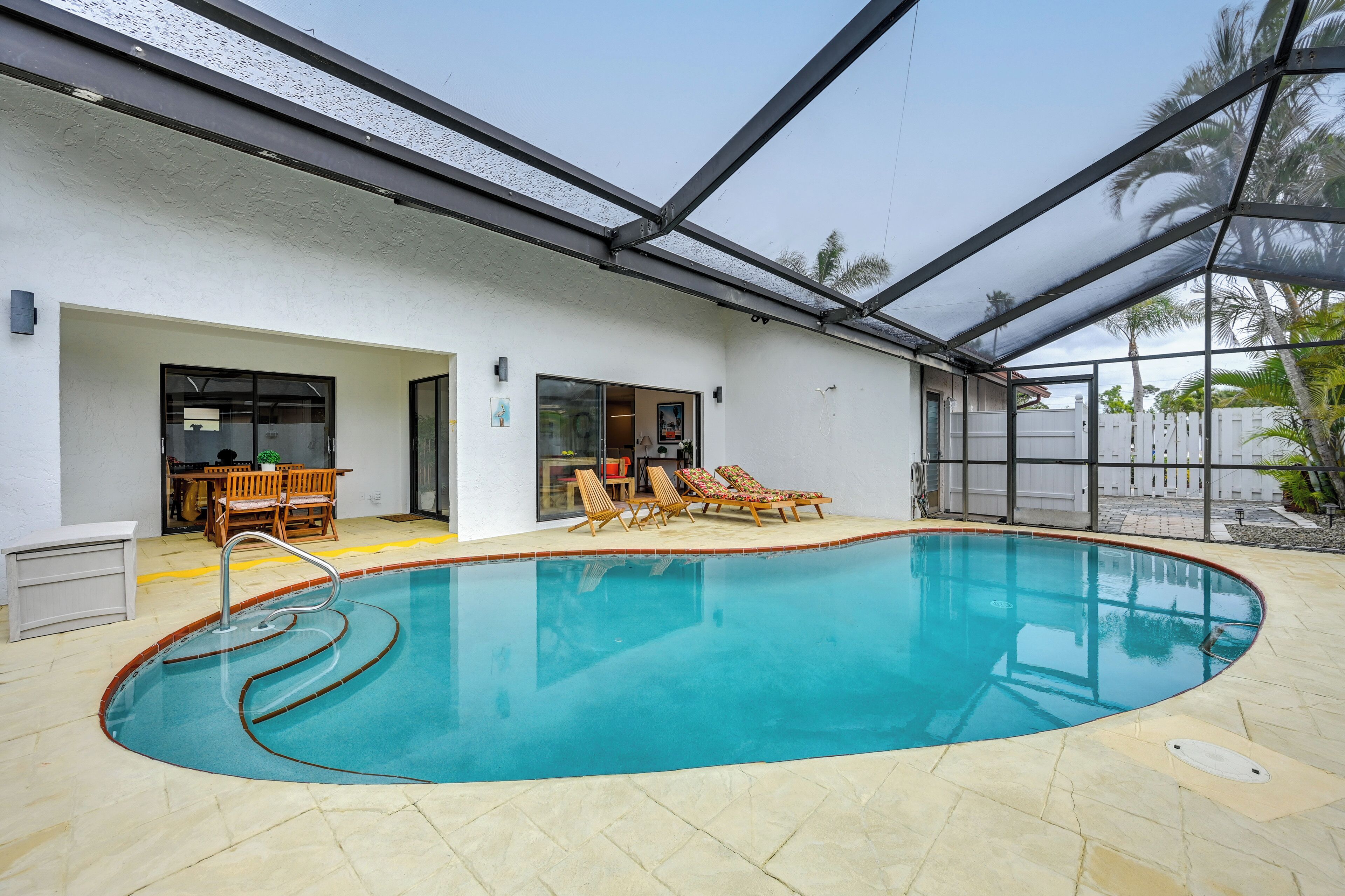 A swimming pool with a glass enclosure, lounge chairs, and a patio area.