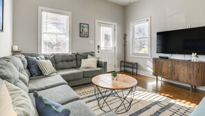A modern living room with a grey sectional sofa, a wooden coffee table, and a TV on a wooden cabinet. - 1 Mi to Dtwn: Home w/ Backyard in Raleigh! (Raleigh)