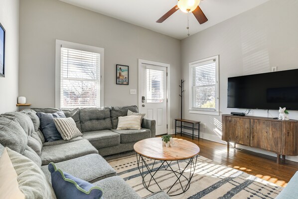 A modern living room with a grey sectional sofa, a wooden coffee table, and a TV on a wooden cabinet. - 1 Mi to Dtwn: Home w/ Backyard in Raleigh! (Raleigh)