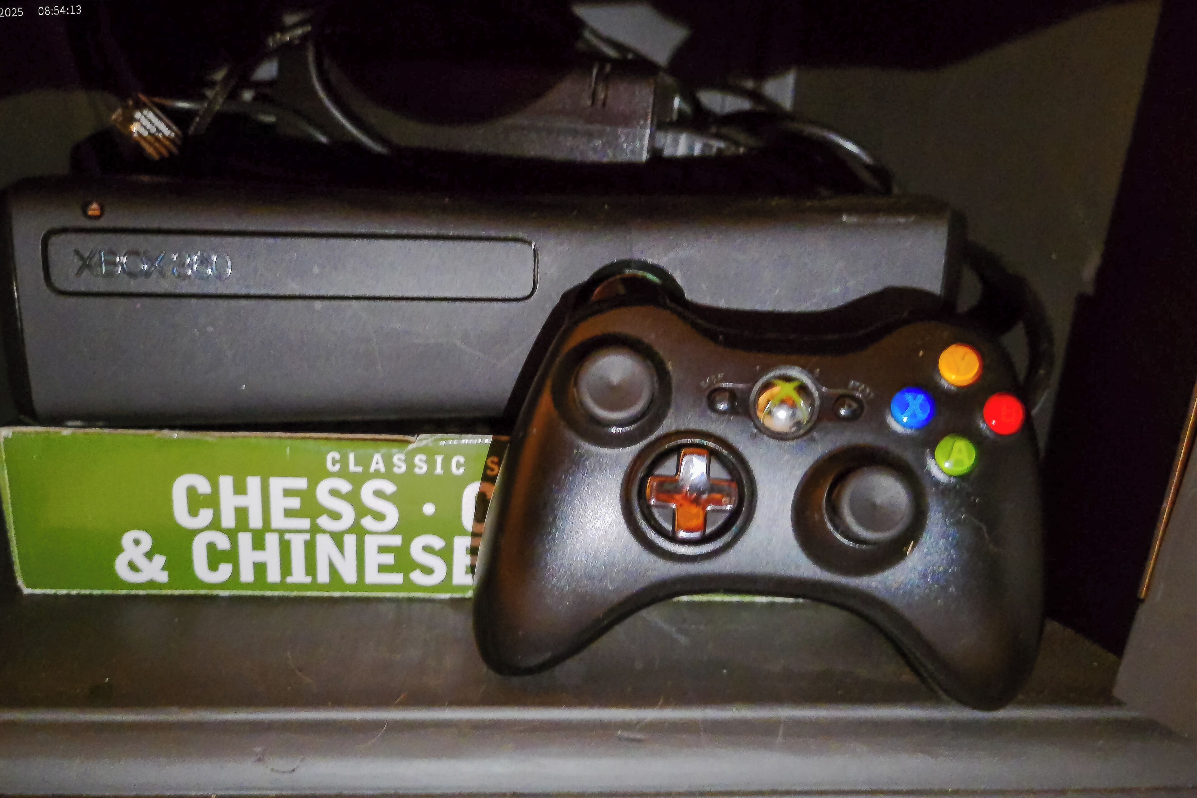 Une manette Xbox 360 noire, à côté d’une boîte verte portant l’inscription « CLASSIC CHESS & CHINESE ».