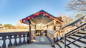 A covered pedestrian bridge with a wooden walkway and metal railing, leading to a building with a sloped roof.