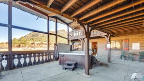 A covered outdoor seating area with a hot tub, wooden beams, and a view of a mountainous landscape.