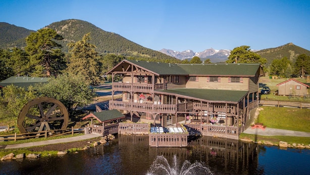 A multi-story wooden lodge with a water wheel and a pond in front.