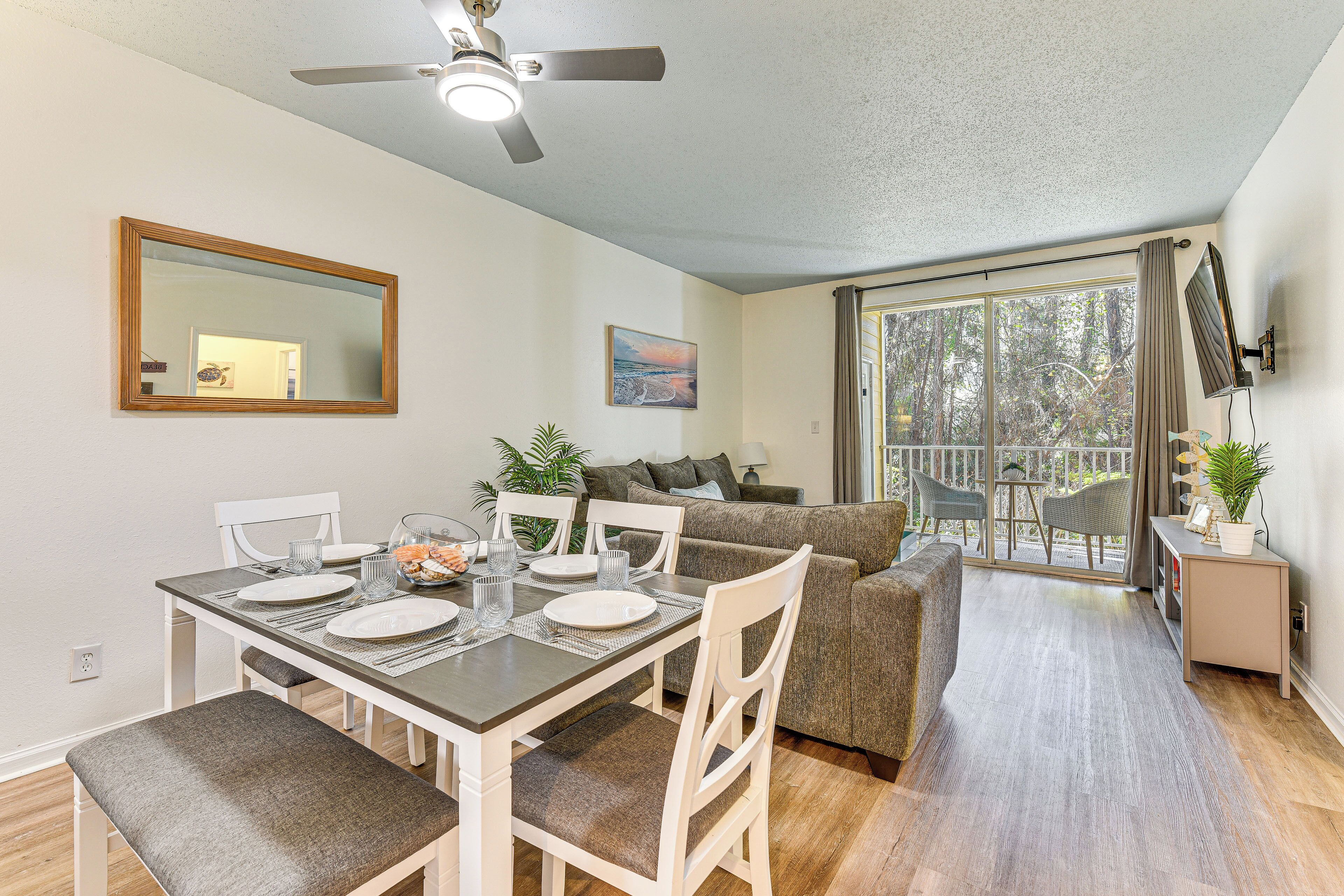 A dining area with a table set for four, a ceiling fan, a large window with curtains, and a view of the outdoors.