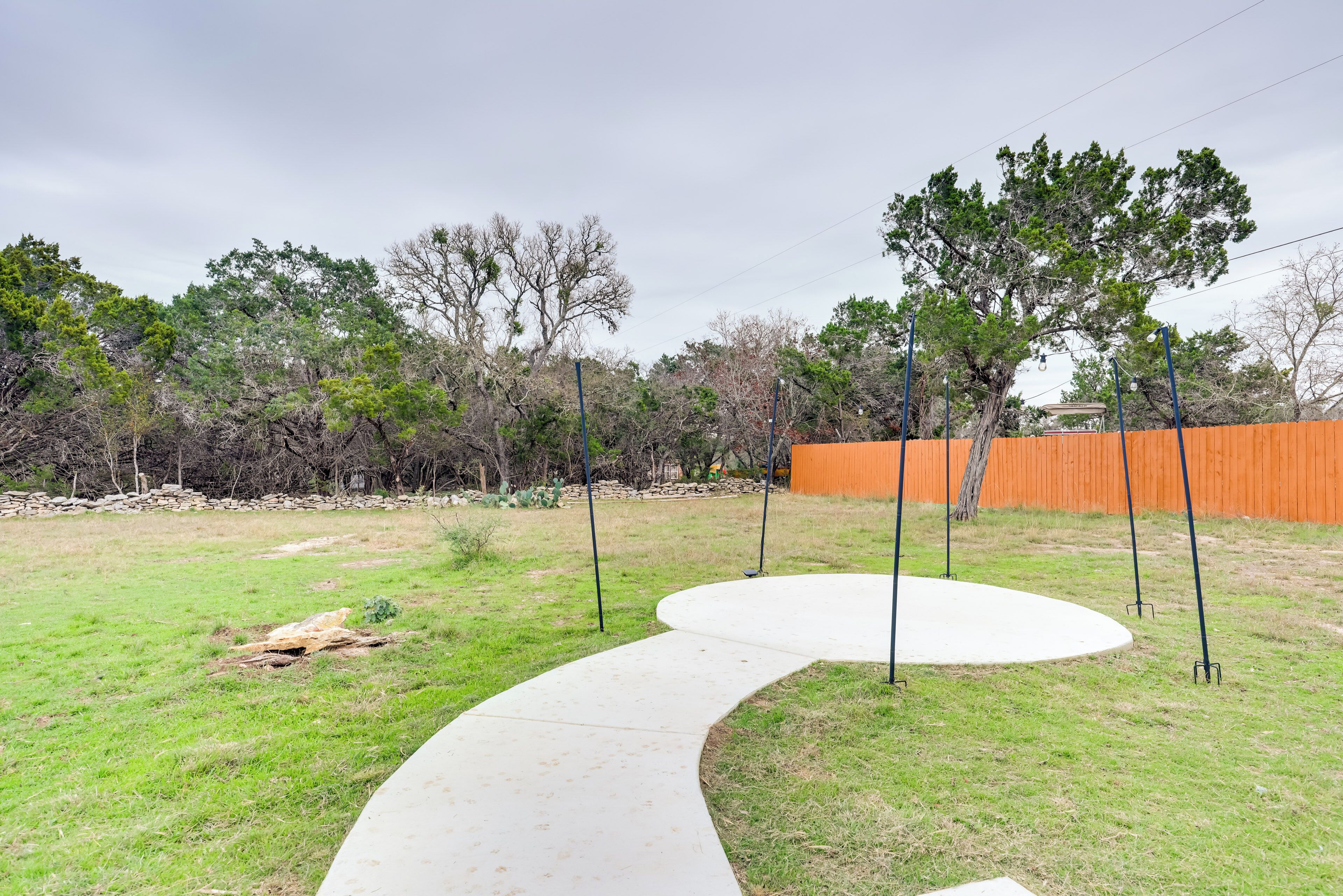 A backyard with a curved concrete path, a wooden fence, and trees.