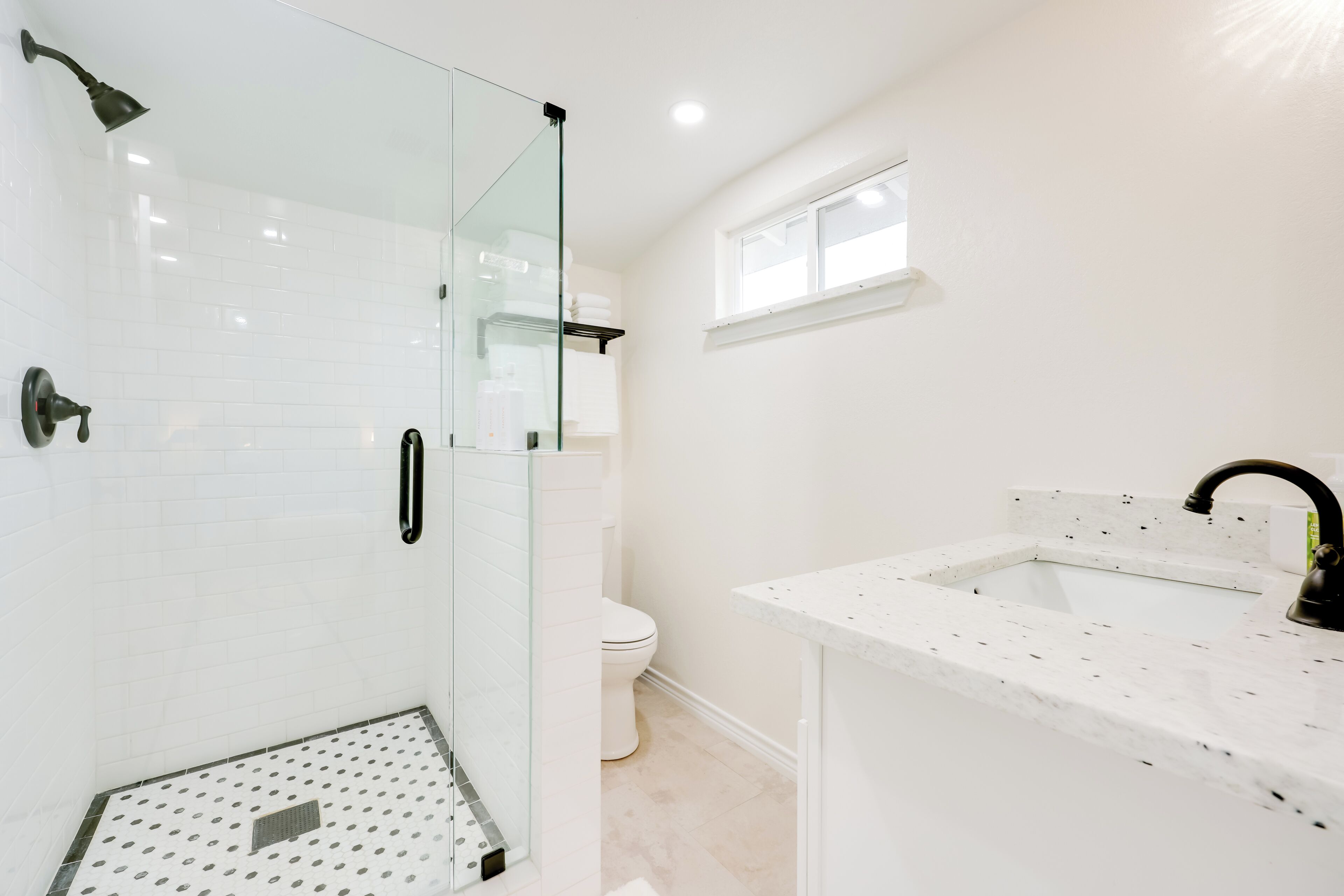 A modern bathroom with a glass-enclosed shower, a white sink with a black faucet, and a toilet.