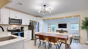 A modern kitchen with white cabinets, stainless steel appliances, a dining area with a wooden table and chairs, and a large window. - 2 Mi to Canyon Lake: Cottage w/ Fire Pit & Grill (Canyon Lake)