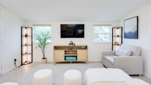 A modern living room with a flat-screen TV, a wooden cabinet, a beige sofa, and a potted plant. - 2 Mi to Canyon Lake: Cottage w/ Fire Pit & Grill (Canyon Lake)