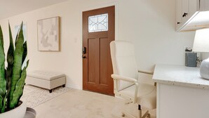 A modern living room with a brown door, a white chair, a white bench, a potted plant, and a framed picture on the wall. - 2 Mi to Canyon Lake: Cottage w/ Fire Pit & Grill (Canyon Lake)