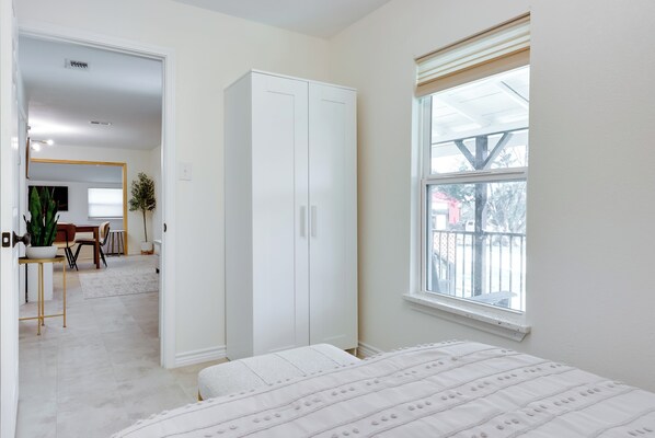 Un dormitorio con cama, armario, ventana con persianas y vistas al exterior.