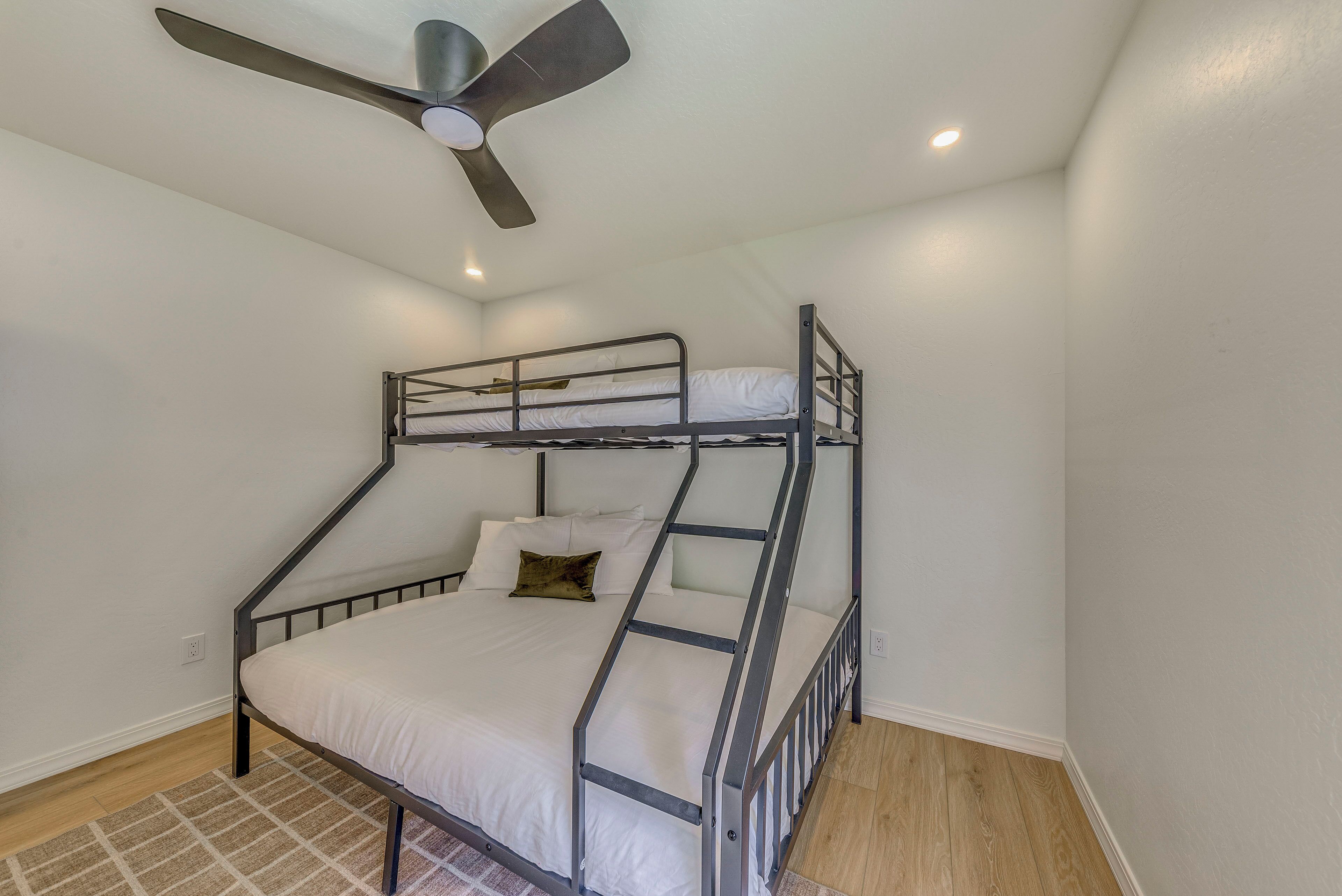 A bunk bed with a ceiling fan and recessed lighting in a room with white walls and wooden flooring.