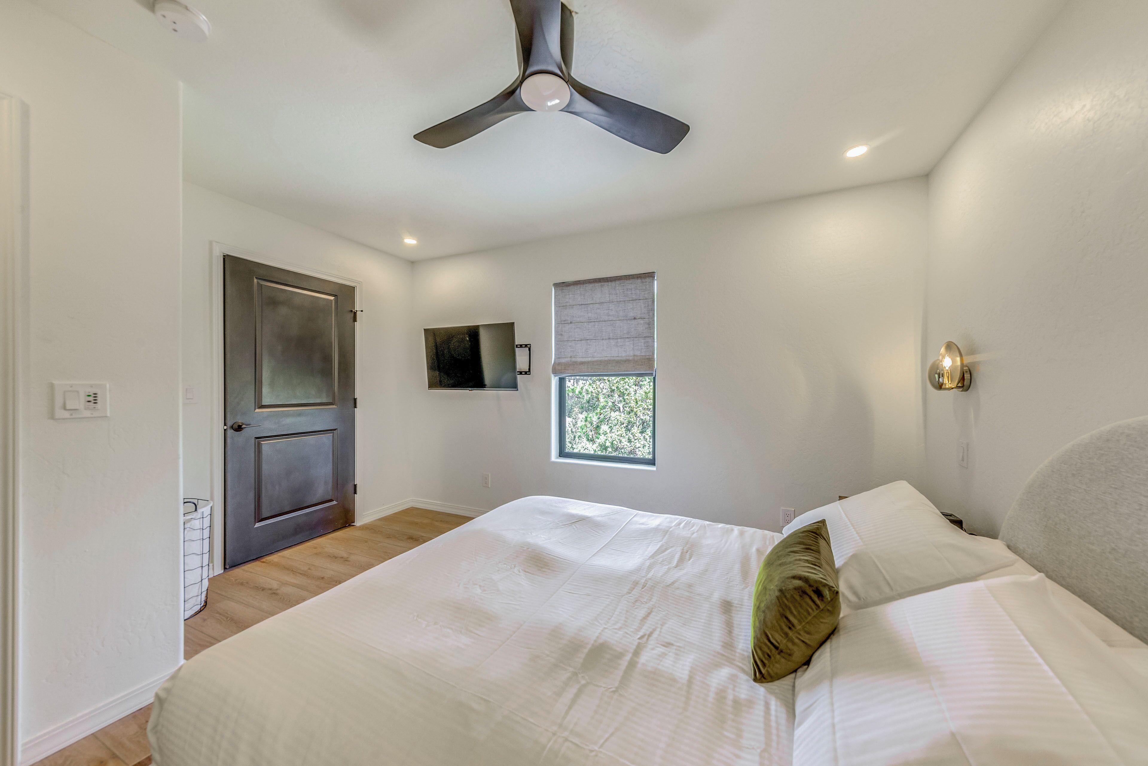 A bedroom with a bed, a ceiling fan, a window, and a door.