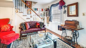 Ein Wohnzimmer mit einem roten Sofa, einem Glastisch und einer Treppe, an deren Wand ein Blumenbild hängt.