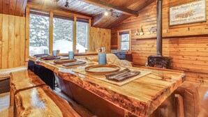 Ein Holzblockhaus-Interieur mit einem großen Holzesstisch, Bänken und einem Kamin.