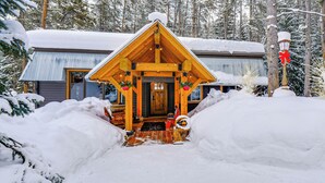 Eine Holzhütte mit einer Veranda, umgeben von schneebedeckten Bäumen.