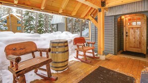 Eine Holzhütte mit einer schneebedeckten Veranda, Holzschaukelstühlen und einem Fass.