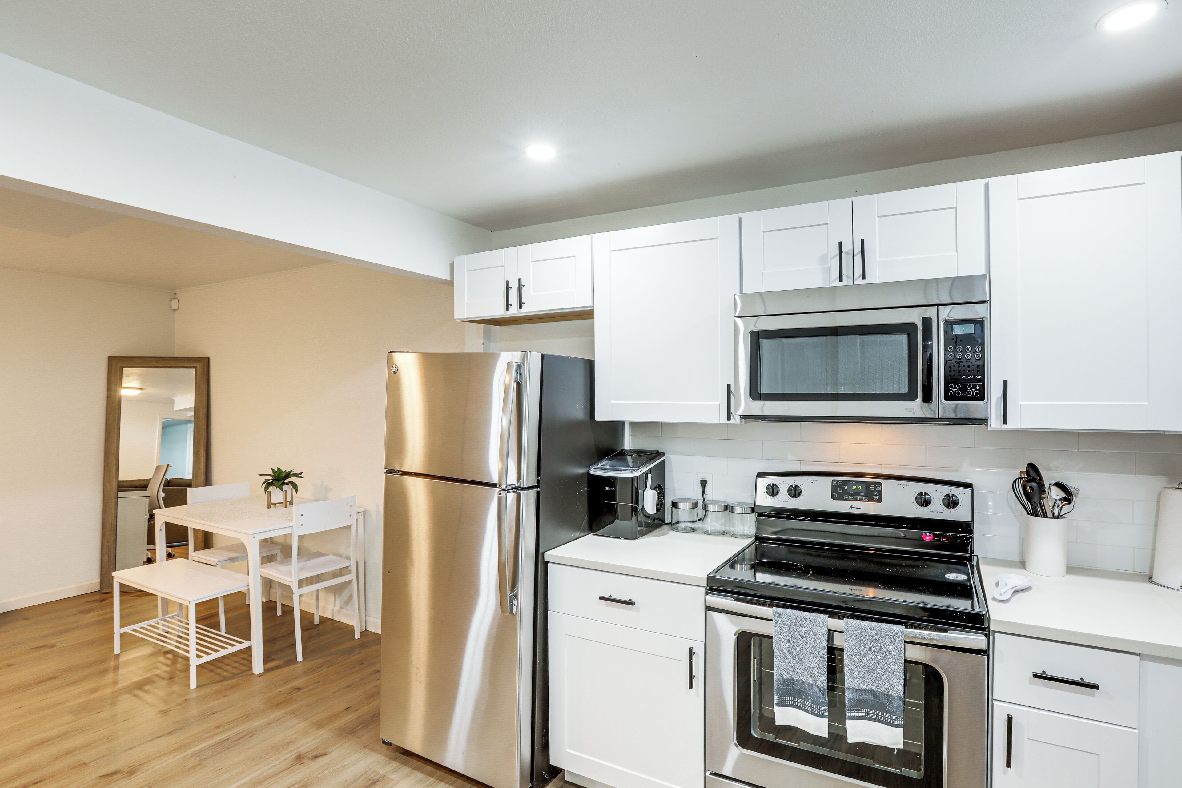 A modern kitchen with white cabinetry, stainless steel appliances, a dining table with chairs, and a small potted plant.
