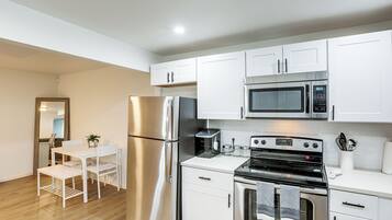 A modern kitchen with white cabinetry, stainless steel appliances, a dining table with chairs, and a small potted plant.