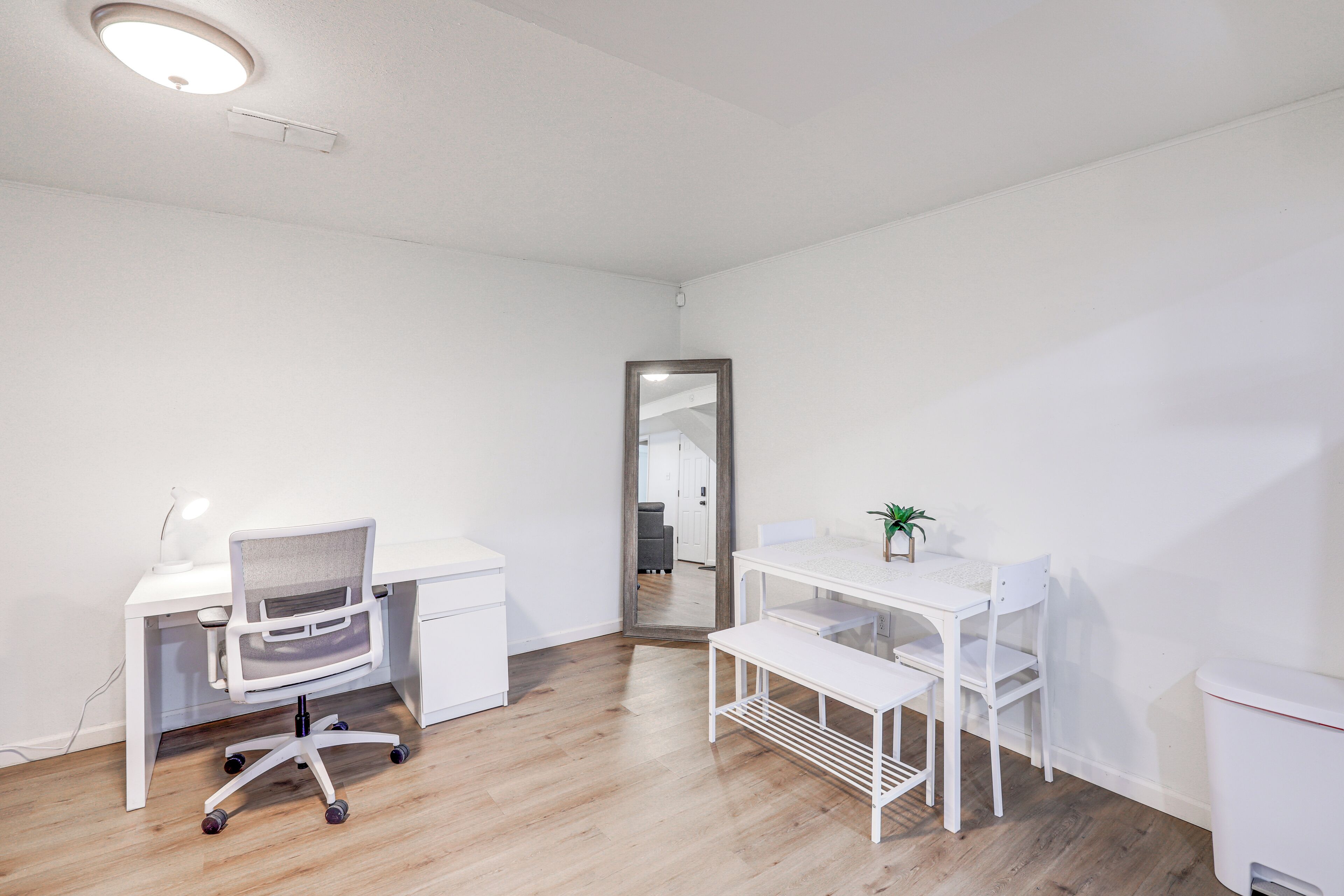 A clean, white room with a desk, chair, and a small table with a plant.