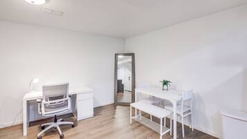 A clean, white room with a desk, chair, and a small table with a plant.