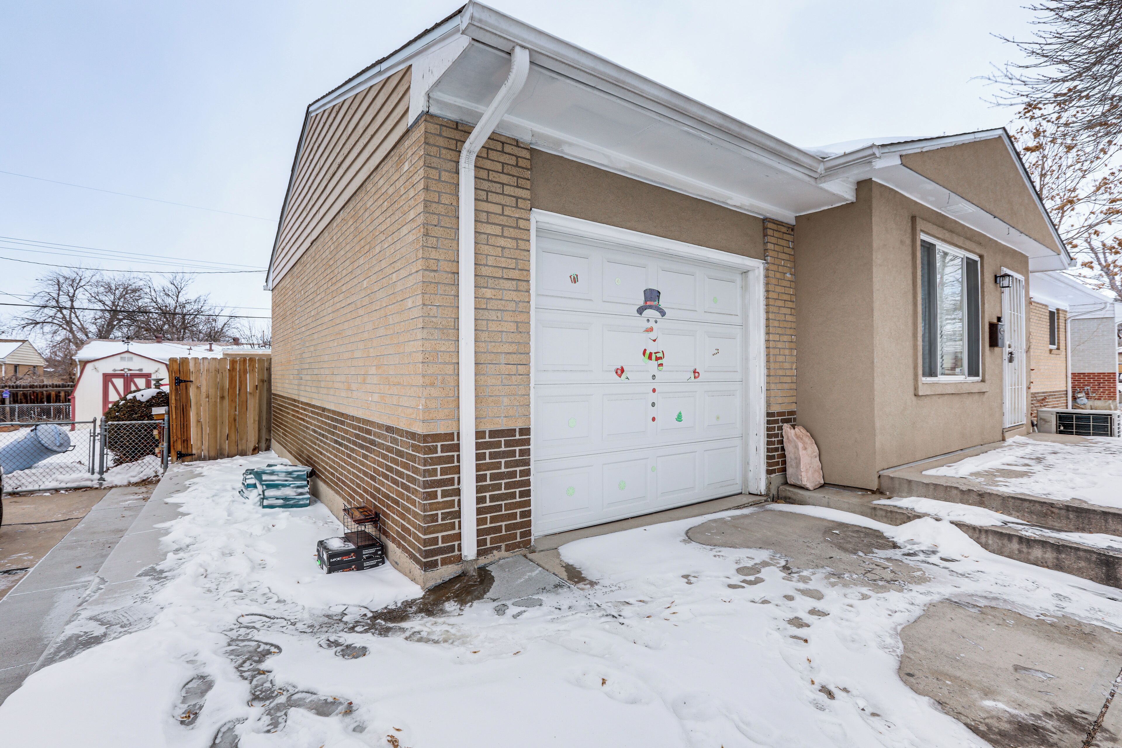 Un garage attenant à une maison, avec une allée enneigée et une façade en briques.