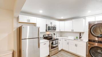 A modern kitchen with stainless steel appliances, white cabinetry, and a built-in washer and dryer.