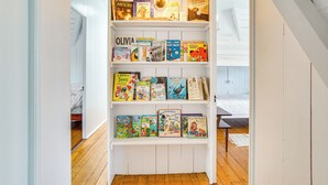 Una estantería con varios libros infantiles, una lámpara y una cama al fondo.