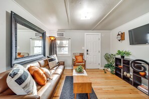 A living room with a brown leather sofa, a wooden coffee table, a large mirror, a TV mounted on the wall, and a bookshelf with decorative items.