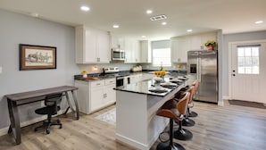 Una cocina moderna con armarios blancos, una isla central con taburetes de bar, un refrigerador de acero inoxidable y un microondas.