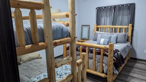 A room with two bunk beds made of wood, a single bed with a headboard, a bedside table, a mirror, and a window with curtains. - Charming 3-bedroom house with WiFi, AC minutes from Lake Oahe/ 3 stall garage (Pierre)