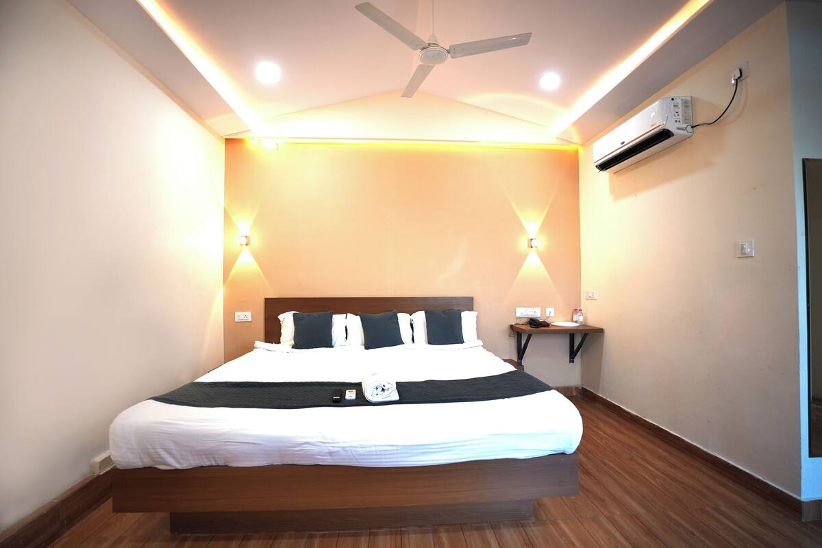 A hotel room with a bed, ceiling fan, wall-mounted air conditioner, bedside lamps, and a nightstand.