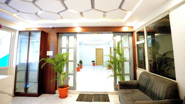 A modern lobby with a hexagonal ceiling, glass doors, a sofa, and potted plants. - Melody mings (Hyderabad)
