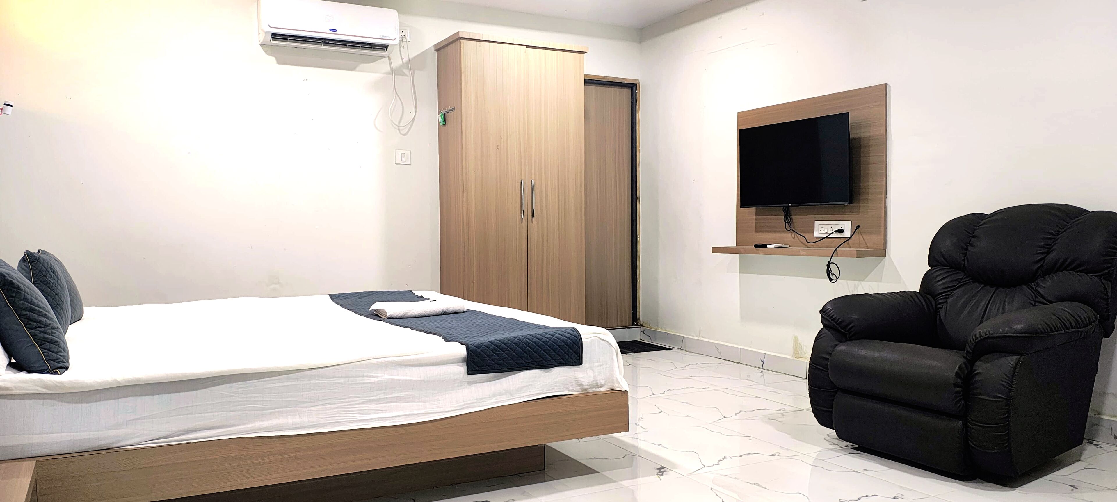 Un dormitorio con cama, armario, sillón de masaje, televisor y aire acondicionado.