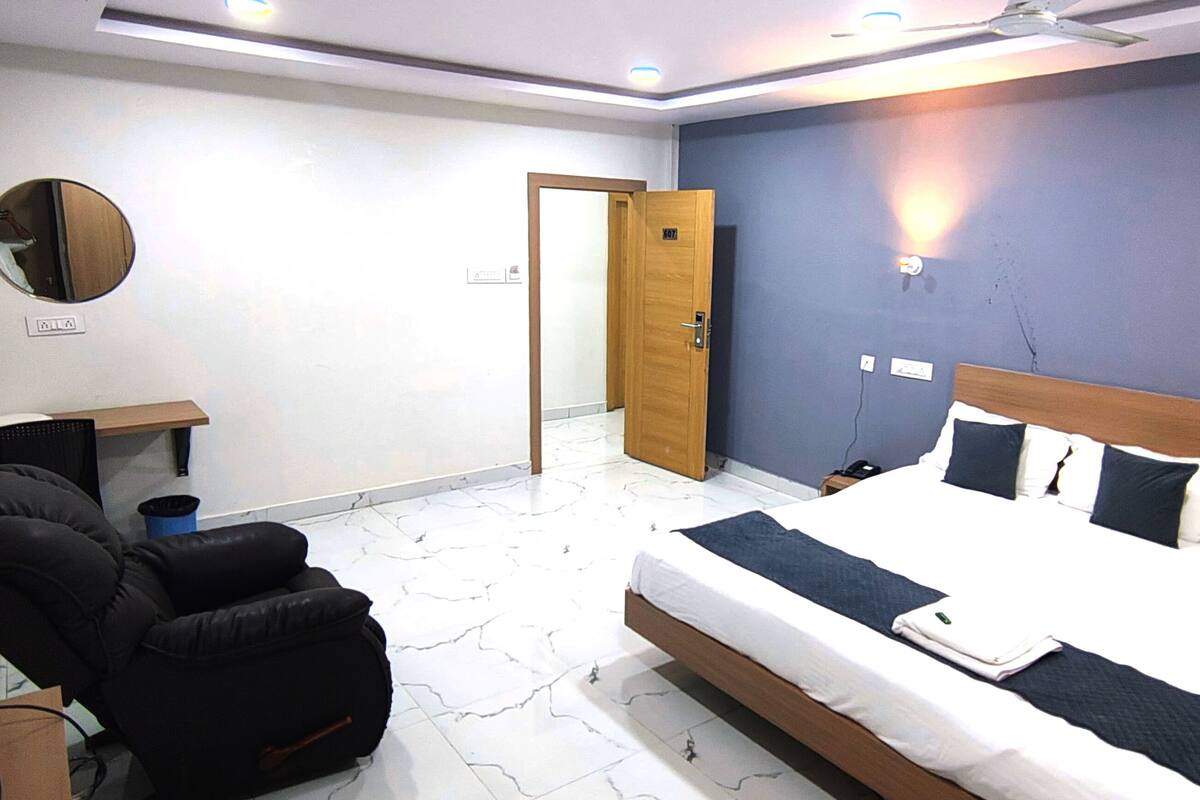A bedroom with a bed, a massage chair, a desk, and a mirror.