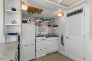 Cocina compacta con muebles blancos, estufa, horno microondas y pileta. Hay luces colgantes y un estante de madera sobre la estufa.