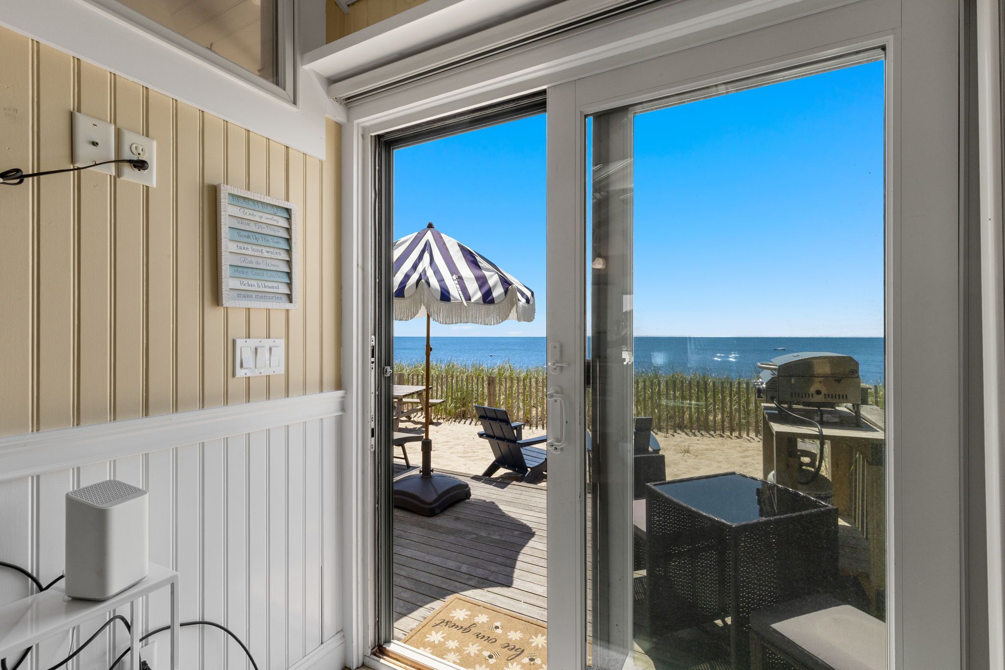 A beachside room with a sliding glass door, a beach umbrella, outdoor seating, and a view of the ocean.