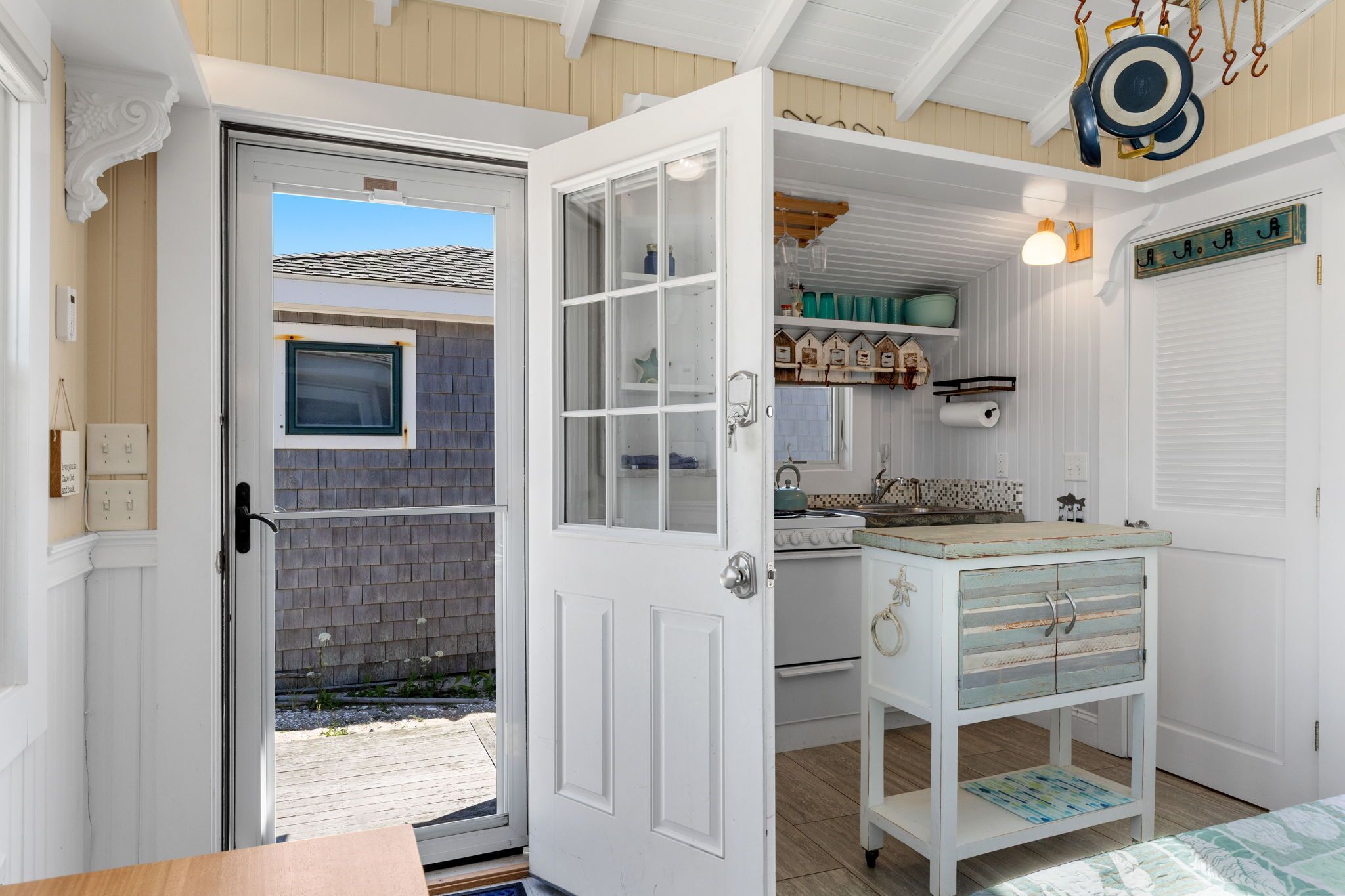 A kitchen with a white door, a window, and a shelf with kitchenware.