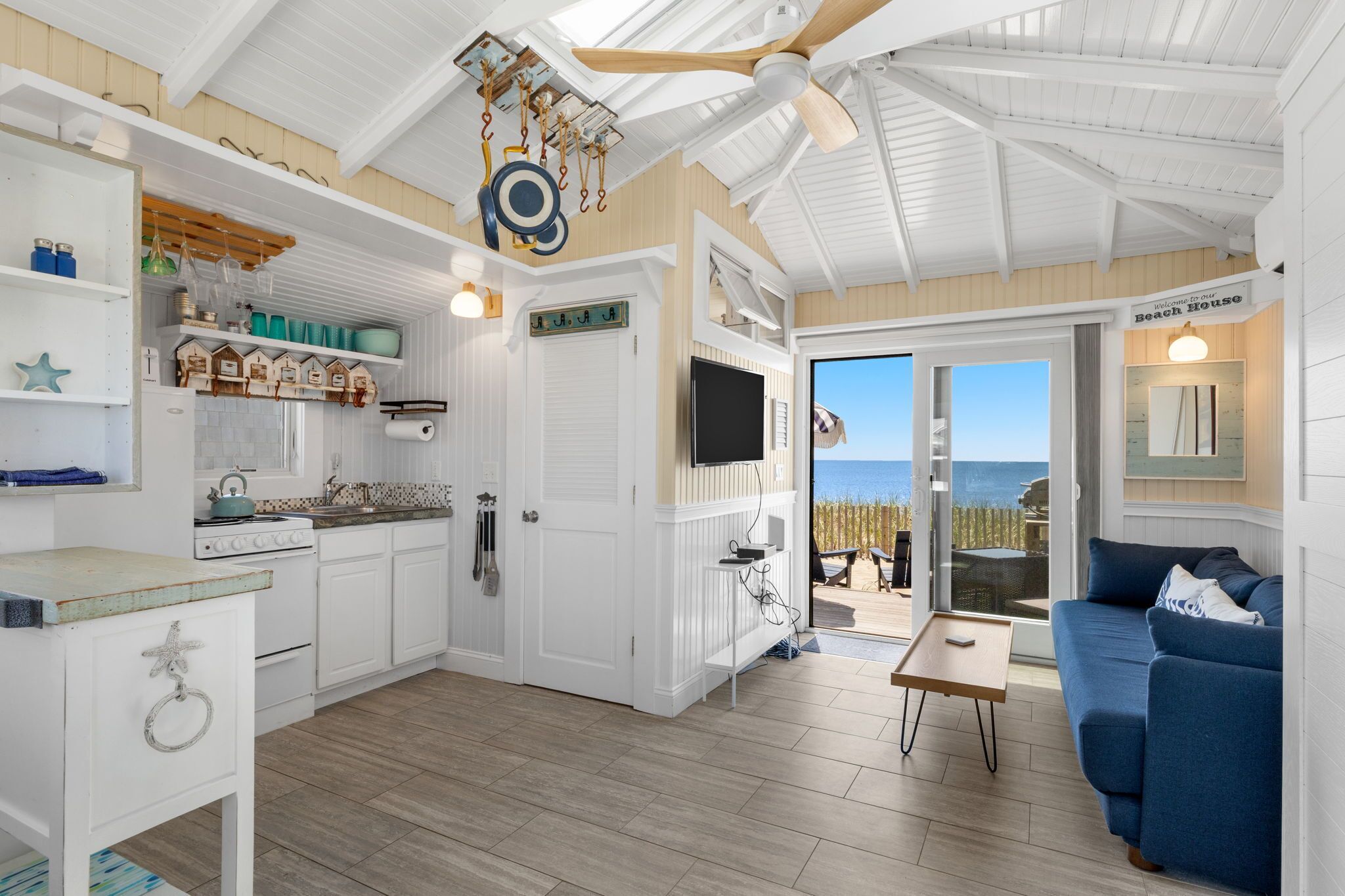 A beach house interior with a kitchen, dining area, and a seating area with a view of the ocean.