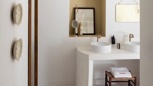 Une salle de bain moderne avec un grand miroir, deux lavabos, un tableau encadré et un petit tabouret en bois.